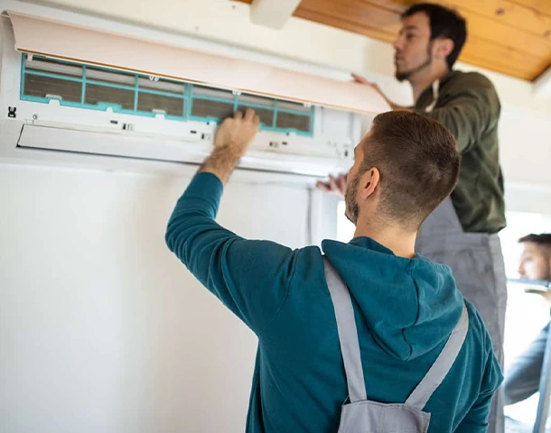 Technicians performing AC installation and maintenance on a wall-mounted unit.