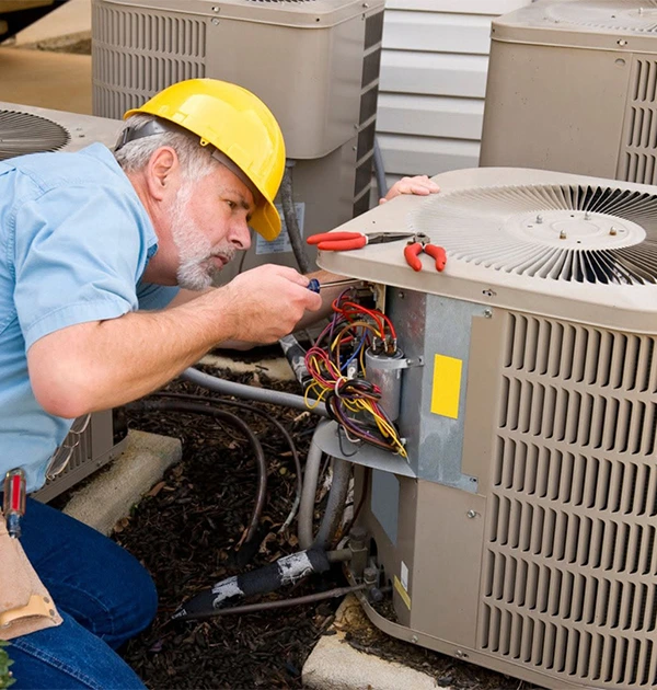 Technician performing AC repair on outdoor unit with tools and wires.